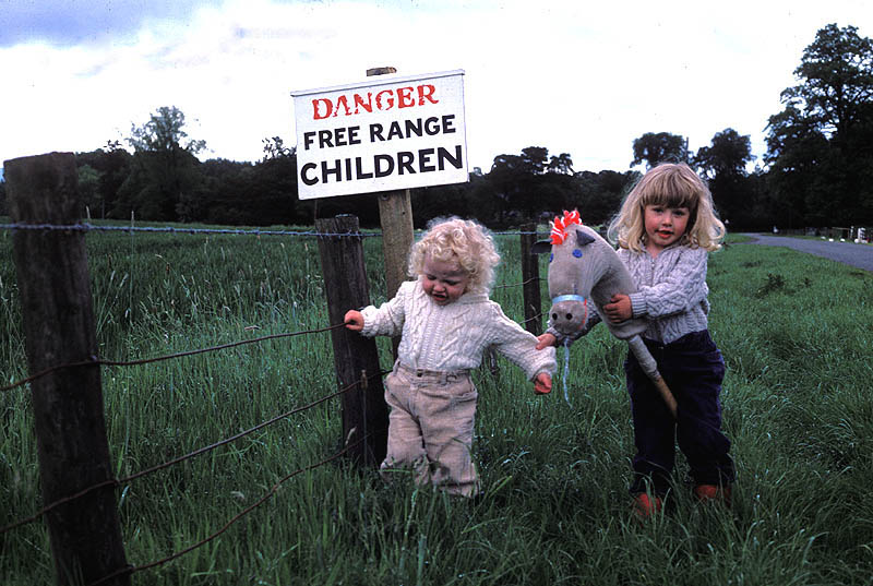 two little girls standing next to a sign that reads "danger free range children"