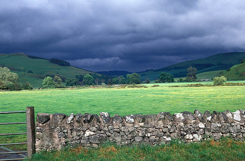 dark clouds over a field with a stone fence around it